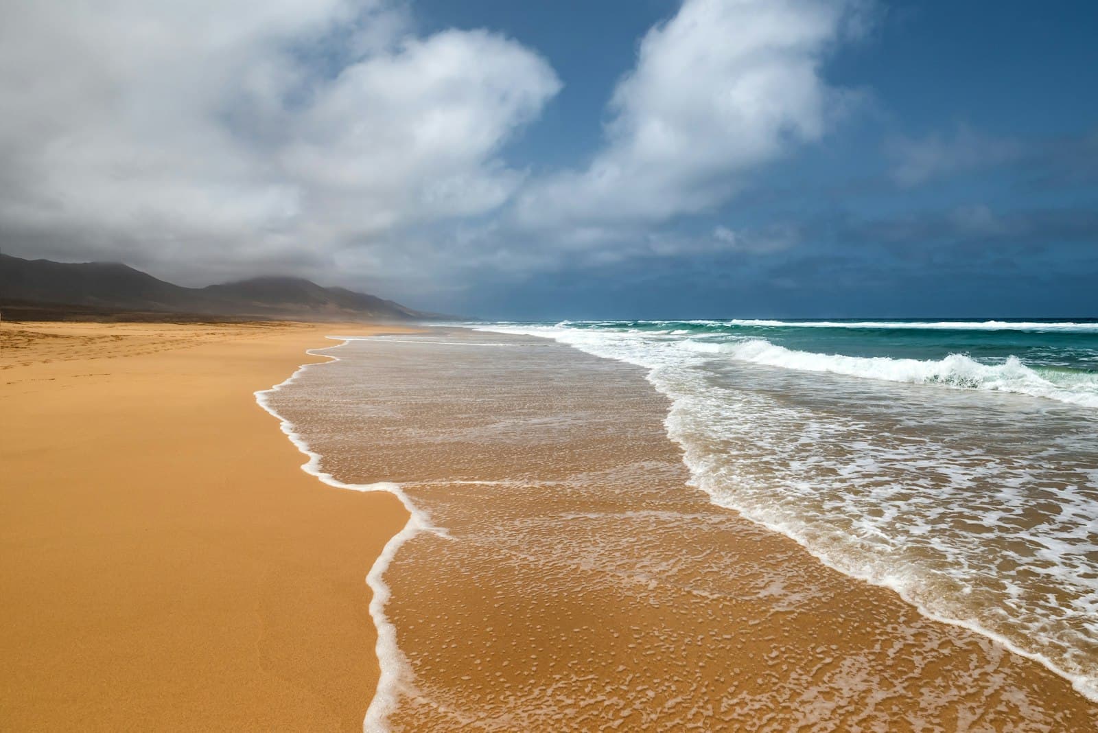 A sandy Canary beach with waves running up the shore.