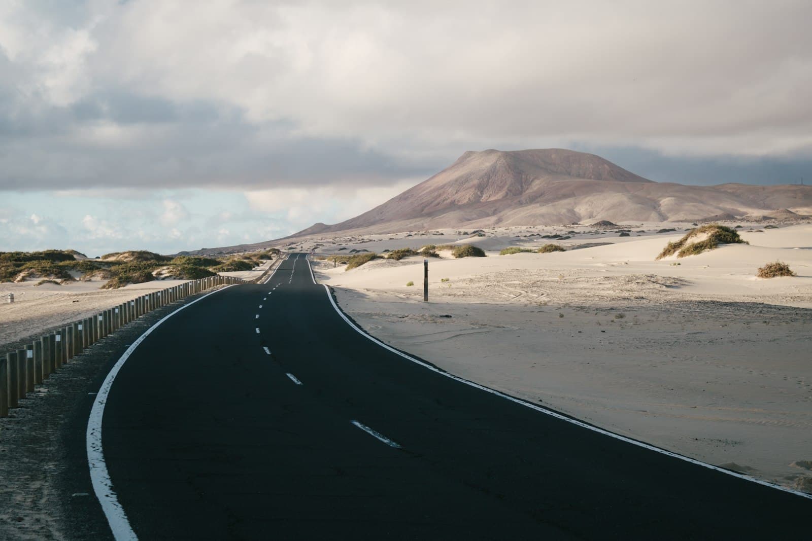 A road crossing pale sand with low hills in the distance.