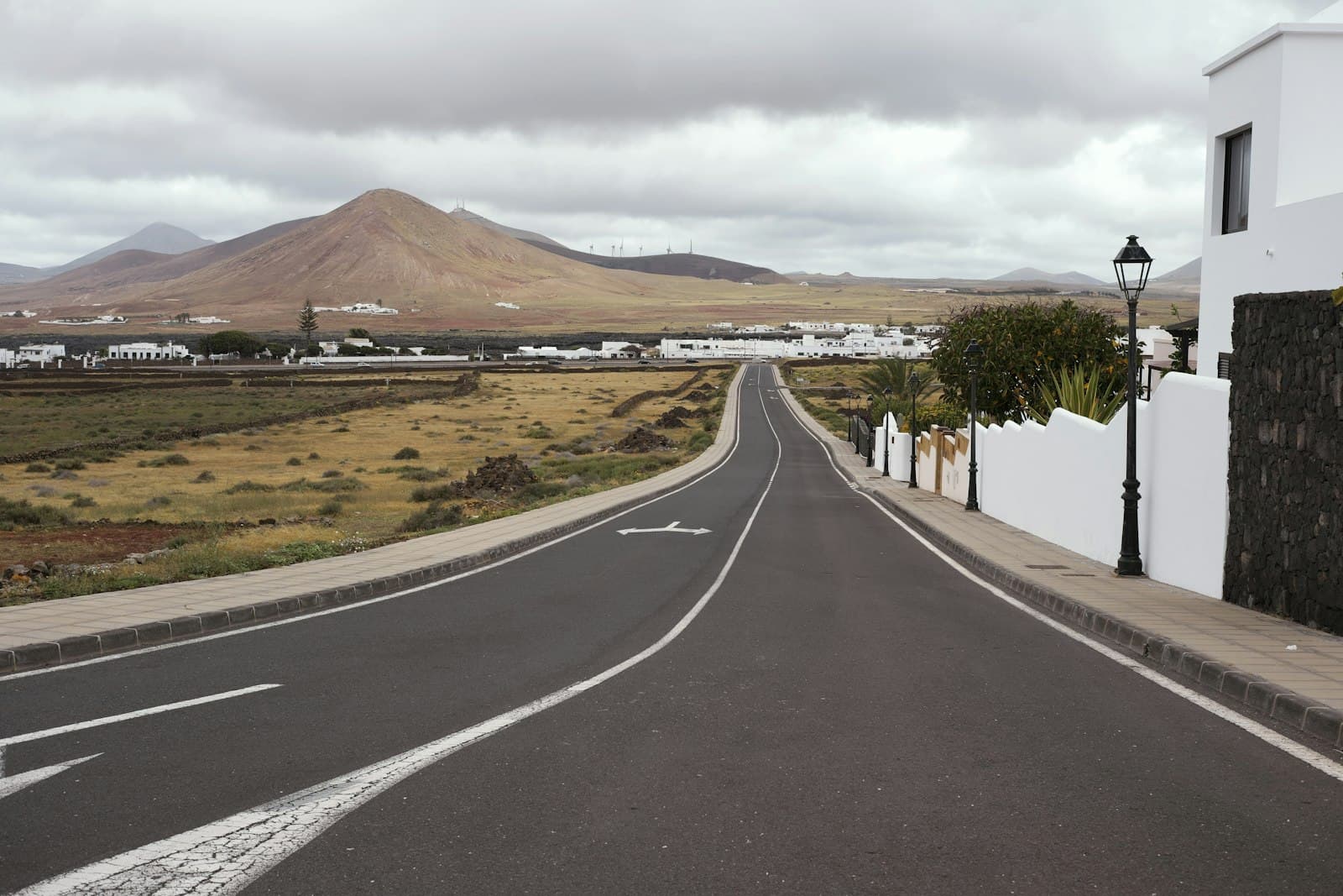 An empty road running towards distant volcanic hills under cloud.