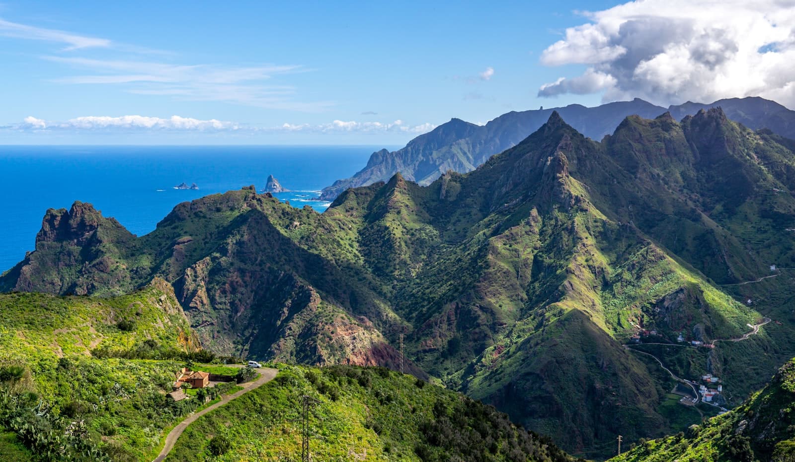 Ridges of green mountains falling away to the sea under a clear sky.