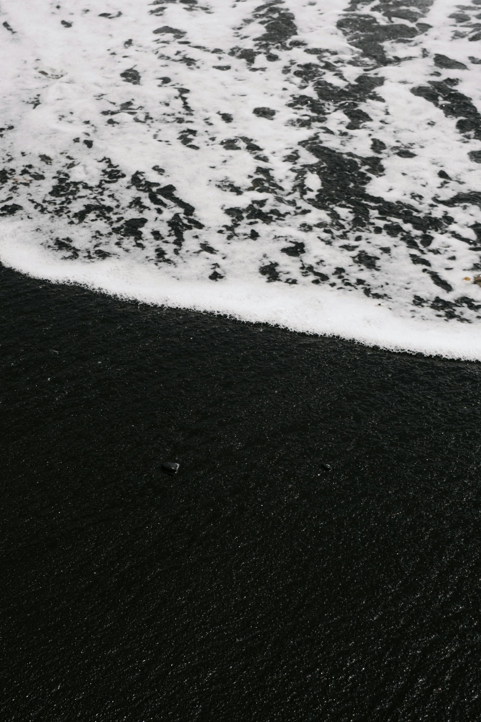 A black sand beach on the Canary coast, with a wave running up the shore.