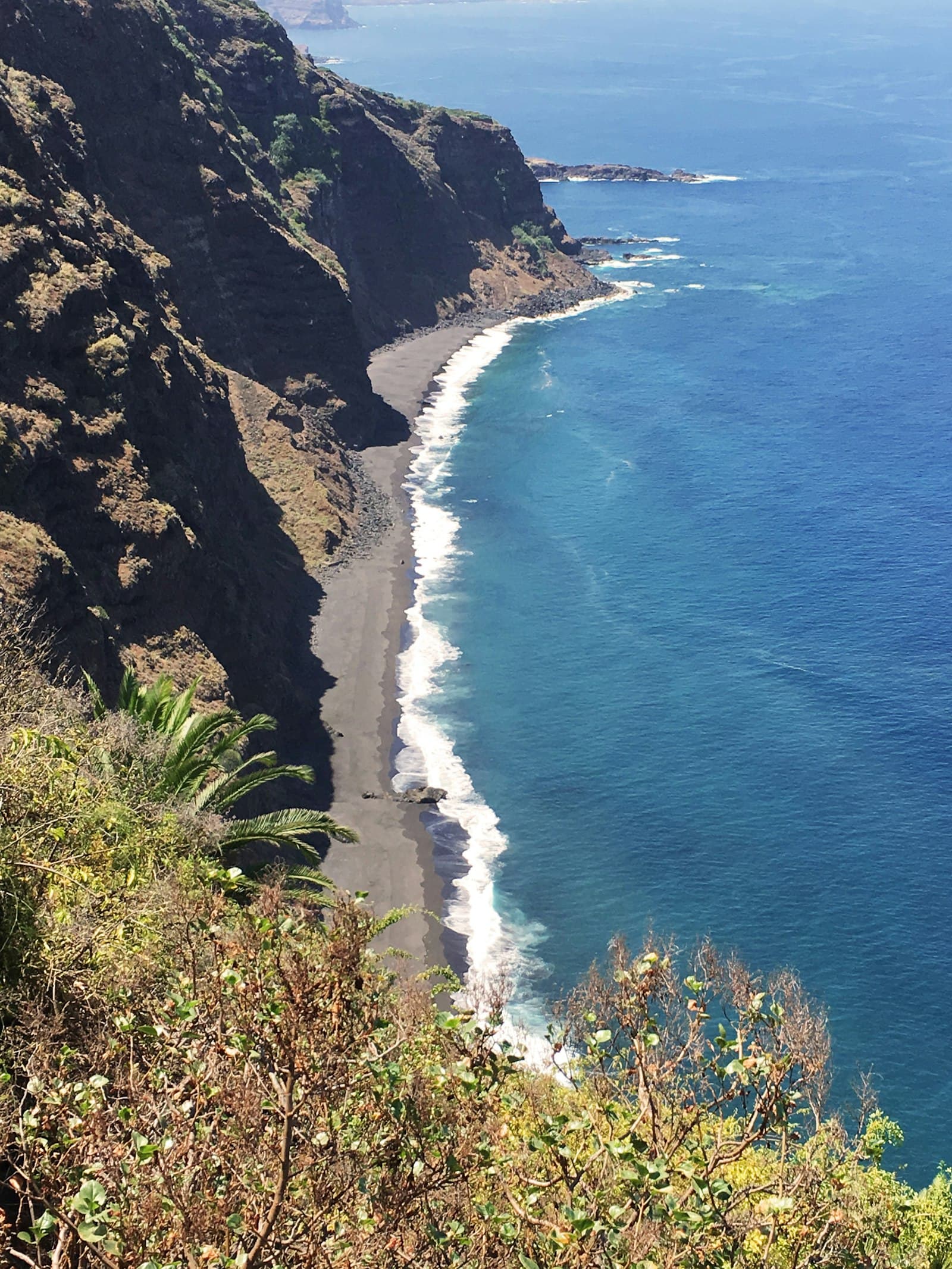 A steep mountain cliff dropping to the shoreline, with a path along its base.