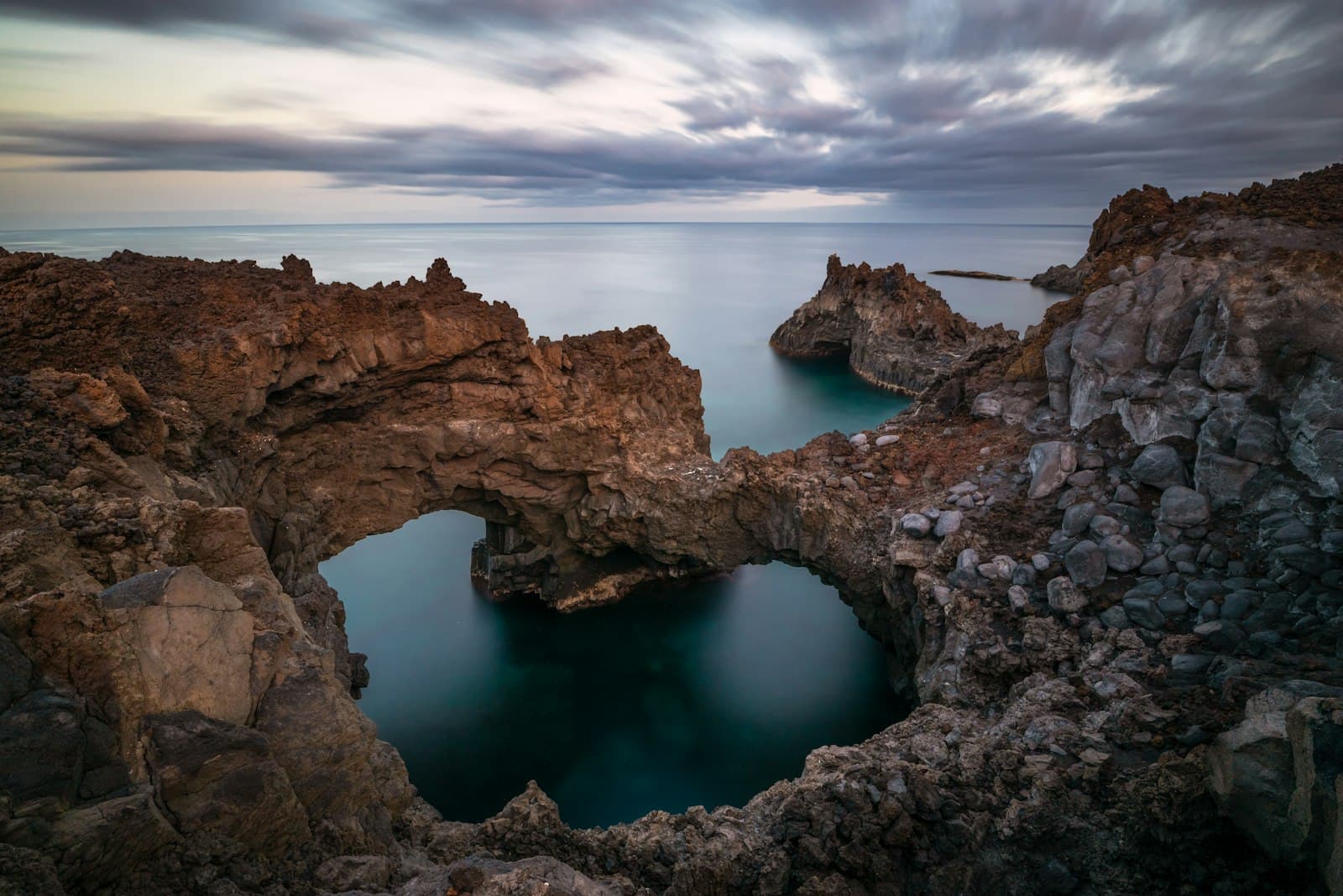 A rocky Canary coastline with natural stone arches and calm water beyond.