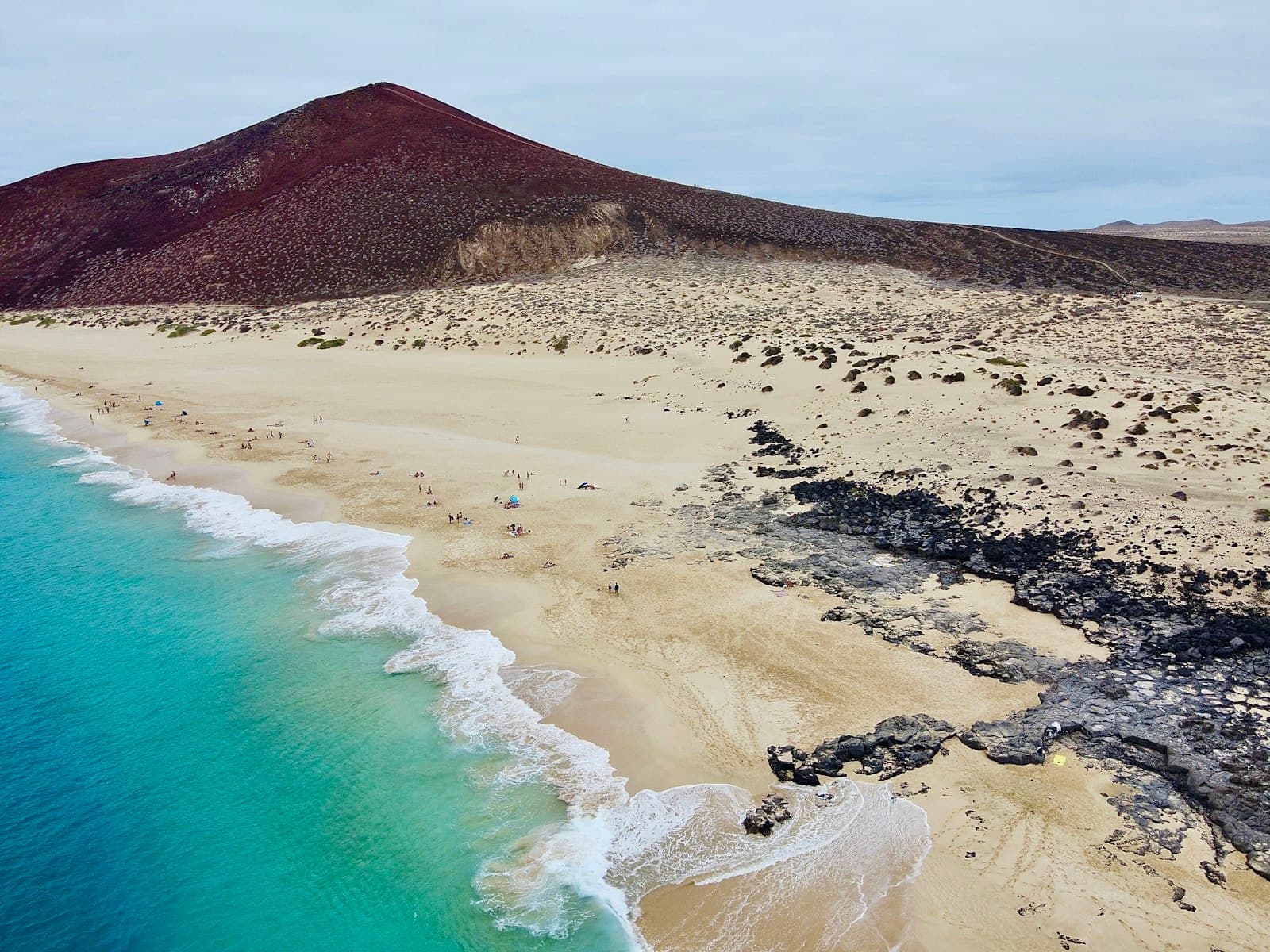A brown volcanic mountain standing beside calm open water.